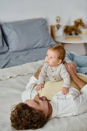hombre con el pelo rizado y la barba abrazando a su hijo en una cama, vinculación entre padre e hijo