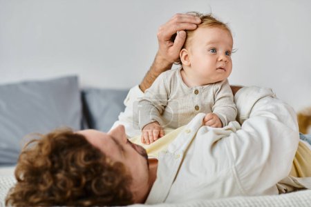 single father with curly hair and beard stroking hair of his infant son in bedroom, love and care
