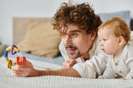 Alleinerziehender Vater und Säugling fasziniert von bunter Rassel im Schlafzimmer, Verbindung zwischen Eltern und Kind