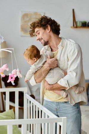 Photo for Smiling father with curly hair and beard holding his infant son near white baby crib at home - Royalty Free Image