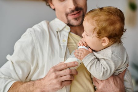 gestutzter Vater mit Bart füttert seinen kleinen Sohn mit nahrhafter Milch aus der Babyflasche und pflegt