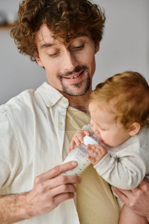 aufmerksamer Vater mit Bart, der seinen kleinen Sohn mit nahrhafter Milch aus der Babyflasche füttert,