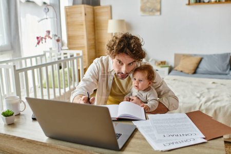 Mann hält seinen kleinen Sohn in den Armen, während er Notizen macht und von zu Hause aus arbeitet, Work-Life-Balance