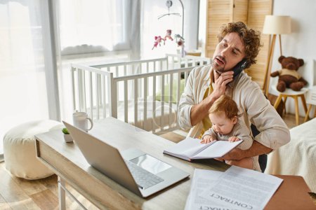 man holding in arms infant son while talking on smartphone and working from home, work-life balance