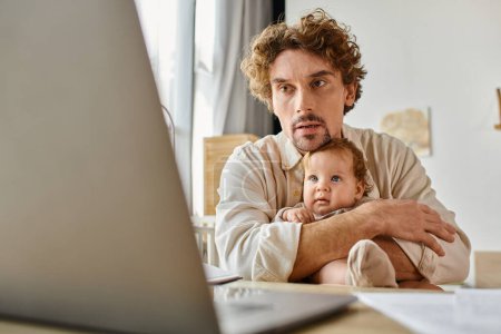 busy single father holding his cute infant baby in hands while working from home, work-life balance