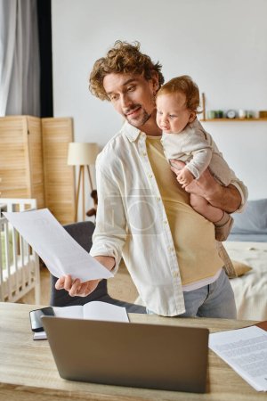 happy and bearded father holding in arms infant child and looking at document, work life balance