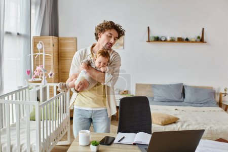 caring single father holding son with baby bottle and looking at laptop on desk, work life balance