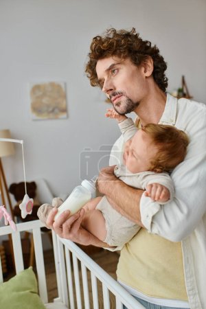 curly-haired father feeding his infant son from baby bottle near crib, fatherhood and care