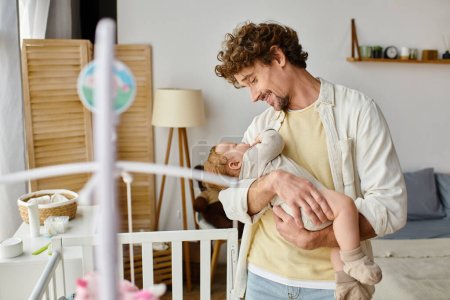 Photo for Happy single father holding in arms his infant son near baby crib in nursery, fatherhood and love - Royalty Free Image