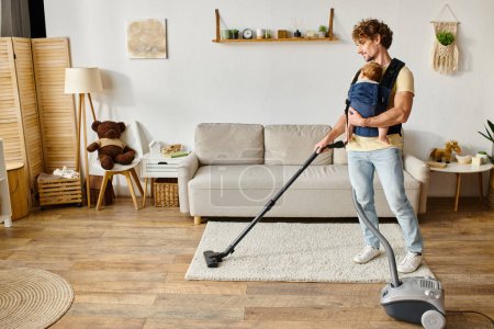 bearded man with infant baby boy in carrier vacuuming apartment at home, fatherly love and housework