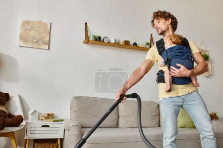 curly father with infant baby boy in carrier vacuuming living room, cleanliness and housework