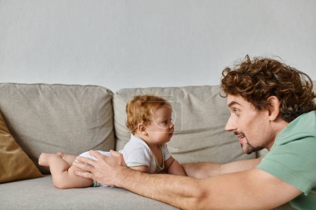 father and infant baby son having a memorable and happy moment on sofa in living room, parenting