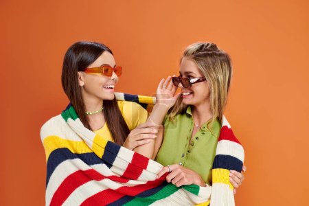 fröhliche entzückende Teenager-Mädchen mit Sonnenbrille, die sich umarmen und mit einer Decke bedecken, Freundschaftstag