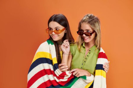 joyous adorable teens with sunglasses covering with blanket and looking away, friendship day