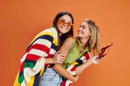 glückliche hübsche Teenager-Mädchen mit Sonnenbrille, die sich umarmen und auf orangefarbenem Hintergrund viel Spaß haben