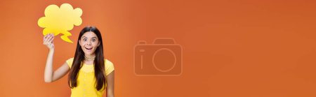 Téléchargez les photos : Adolescent joyeux tenant bulle de pensée jaune et regardant la caméra sur fond orange, bannière - en image libre de droit
