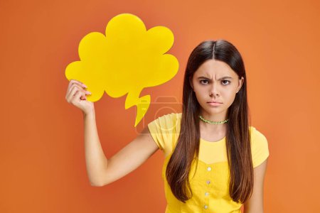 Frustriertes Teenager-Mädchen in lebendigem T-Shirt posiert mit gelber Gedankenblase und blickt in die Kamera