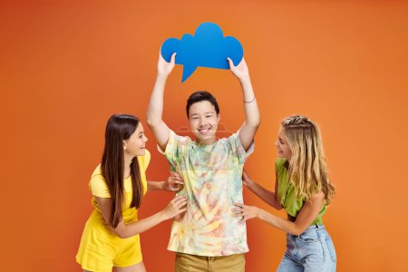 drei fröhliche Teenager in lebendigen Kostümen posieren mit blauer Gedankenblase auf orangefarbenem Hintergrund