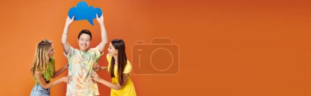 jolly diverse teens posing with blue thought bubble on orange backdrop, friendship day, banner