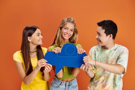 three jolly multiracial teenagers in casual attire holding blue thought bubble, friendship day