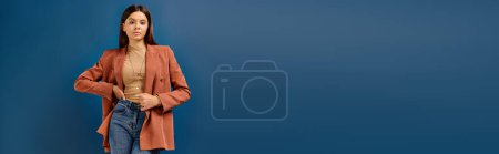 stylish teenage girl in elegant blazer posing on blue backdrop and looking at camera, banner