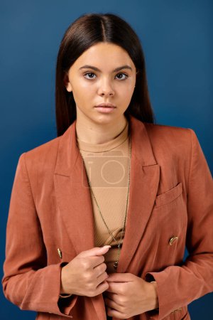adorable teenage girl with long hair in elegant blazer posing on blue backdrop and looking at camera