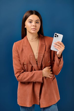 elegant teenage girl in fashionable blazer posing with smartphone in hand and looking at camera
