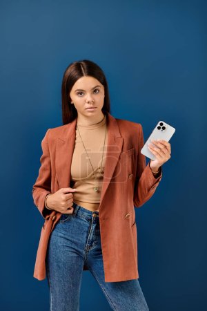 teenage stylish girl in elegant brown blazer posing with mobile phone in hand and looking at camera