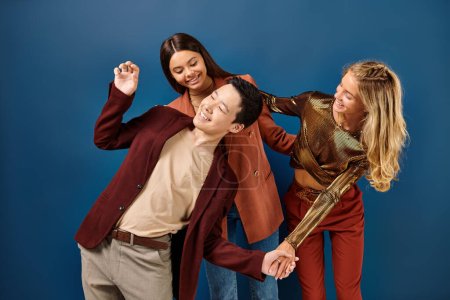 joyful multiracial teenagers in stylish clothes having much fun on blue background, friendship day