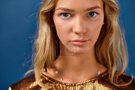 Porträt einer hübschen blonden Teenagerin in lebendiger eleganter Kleidung, die vor blauem Hintergrund in die Kamera blickt
