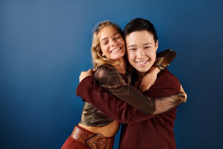 cheerful adolescent blonde girl and asian boy hugging and smiling at camera, friendship day