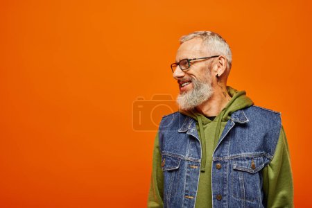 Photo for Joyous handsome mature man in vibrant hoodie and vest with glasses smiling and looking away - Royalty Free Image