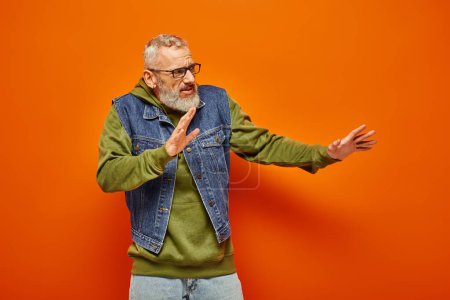 careful handsome mature man with glasses and beard in vibrant hoodie posing and looking away