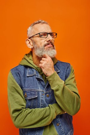 concentrated mature man in vibrant green hoodie and denim vest posing and looking at camera