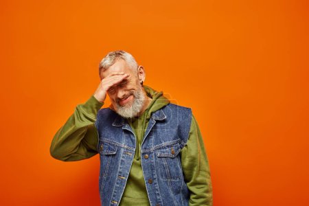 Téléchargez les photos : Joyeux beau mature homme en tenue vive avec barbe grise souriant à la caméra sur fond orange - en image libre de droit