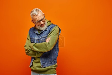 good looking mature man in vibrant attire posing with arms crossed on chest on orange backdrop