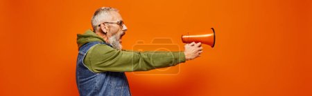 Photo for Attractive mature man in green hoodie and stylish denim vest aiming with megaphone in hands, banner - Royalty Free Image