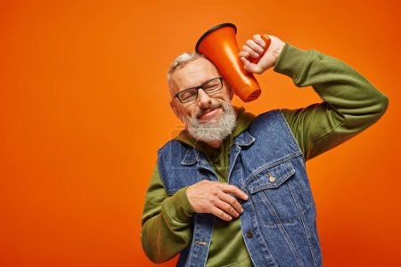 Photo for Cheerful good looking mature man in vibrant attire posing with closed eyes with megaphone near head - Royalty Free Image