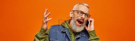 Photo for Handsome jolly mature man in green hoodie and denim vest with glasses talking by phone, banner - Royalty Free Image