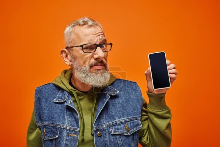 Photo for Confused attractive mature man in vibrant green hoodie holding phone and looking at camera - Royalty Free Image