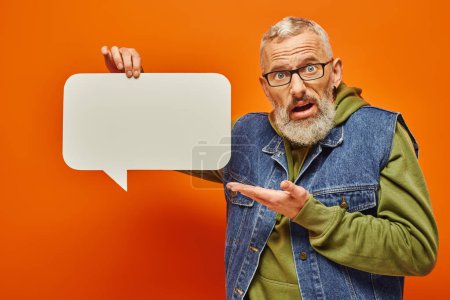 Photo for Confused attractive mature man in fashionable vest holding speech bubble and looking at camera - Royalty Free Image