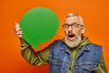 Photo for Shocked handsome mature male model in vibrant attire holding speech bubble and looking at camera - Royalty Free Image
