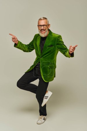 Photo for Handsome cheerful mature man in vibrant green blazer posing on one leg and smiling at camera - Royalty Free Image