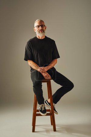 handsome jolly mature male model in black shirt with glasses and tattoos looking at camera