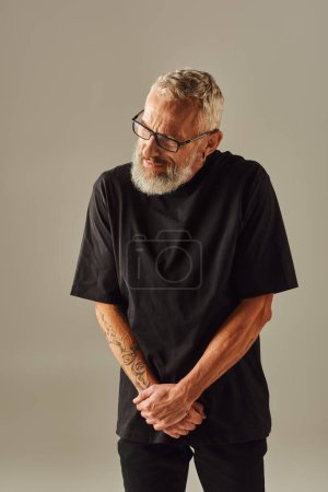attractive mature man with tattoos in black t shirt posing and looking away on beige backdrop