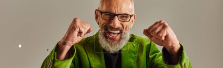 Photo for Jolly mature man in vivid blazer smiling and showing fists at camera on beige background, banner - Royalty Free Image