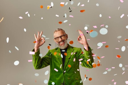Photo for Handsome jolly mature man in green blazer showing okay sign under confetti rain on beige backdrop - Royalty Free Image