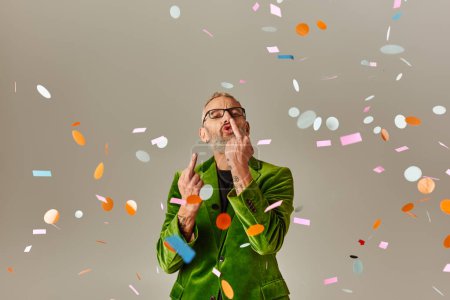 Téléchargez les photos : Cheeky mature homme en vert vibrant blazer montrant majeur doigts à la caméra sous la pluie confettis - en image libre de droit