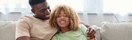 Photo for Cheerful black man embracing happy girlfriend in braces while sitting on cozy couch, banner - Royalty Free Image