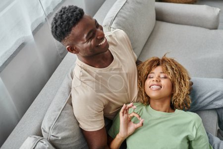 glücklich schwarze Frau zeigt ok Zeichen für Freund, während auf seinem Schoß liegend, mit Seufzer Sprache